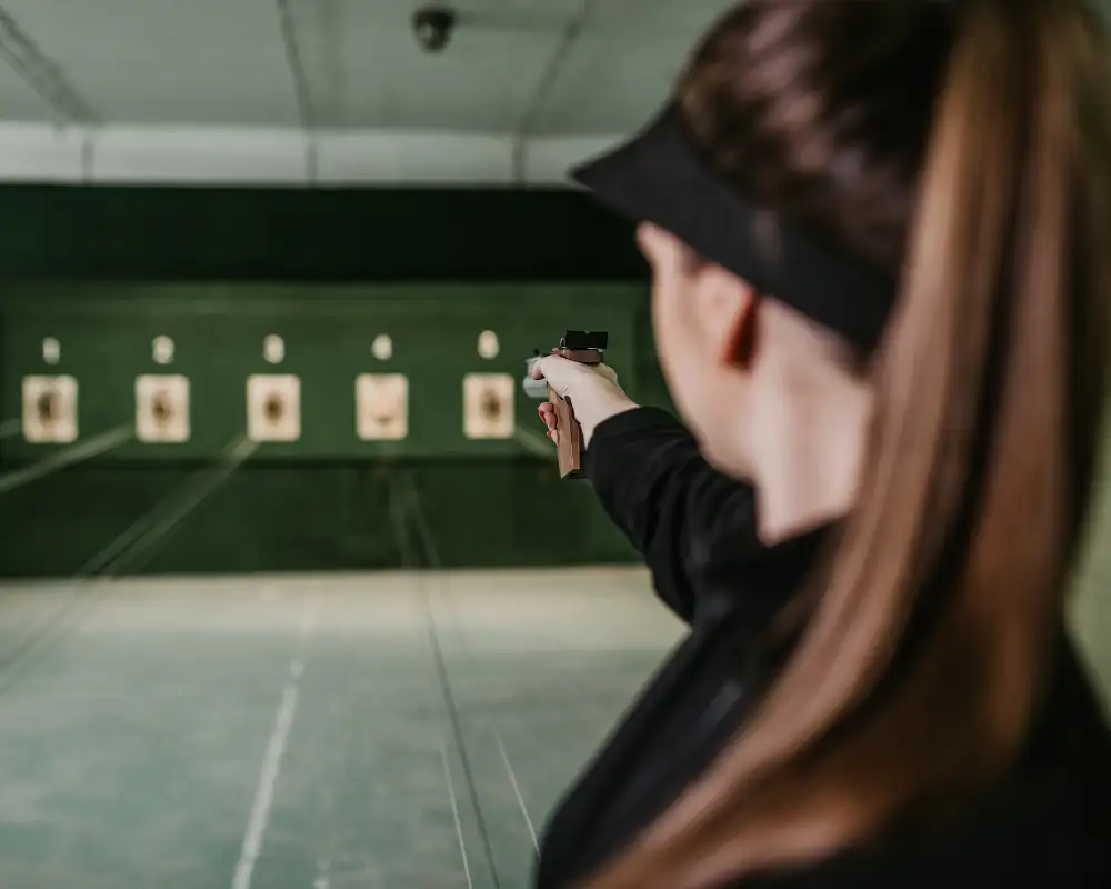 Eine Person im Trainingsanzug zielt mit einer Pistole auf eine Zielscheibe in einer Schießanlage. Die Umgebung ist sauber und gut beleuchtet.